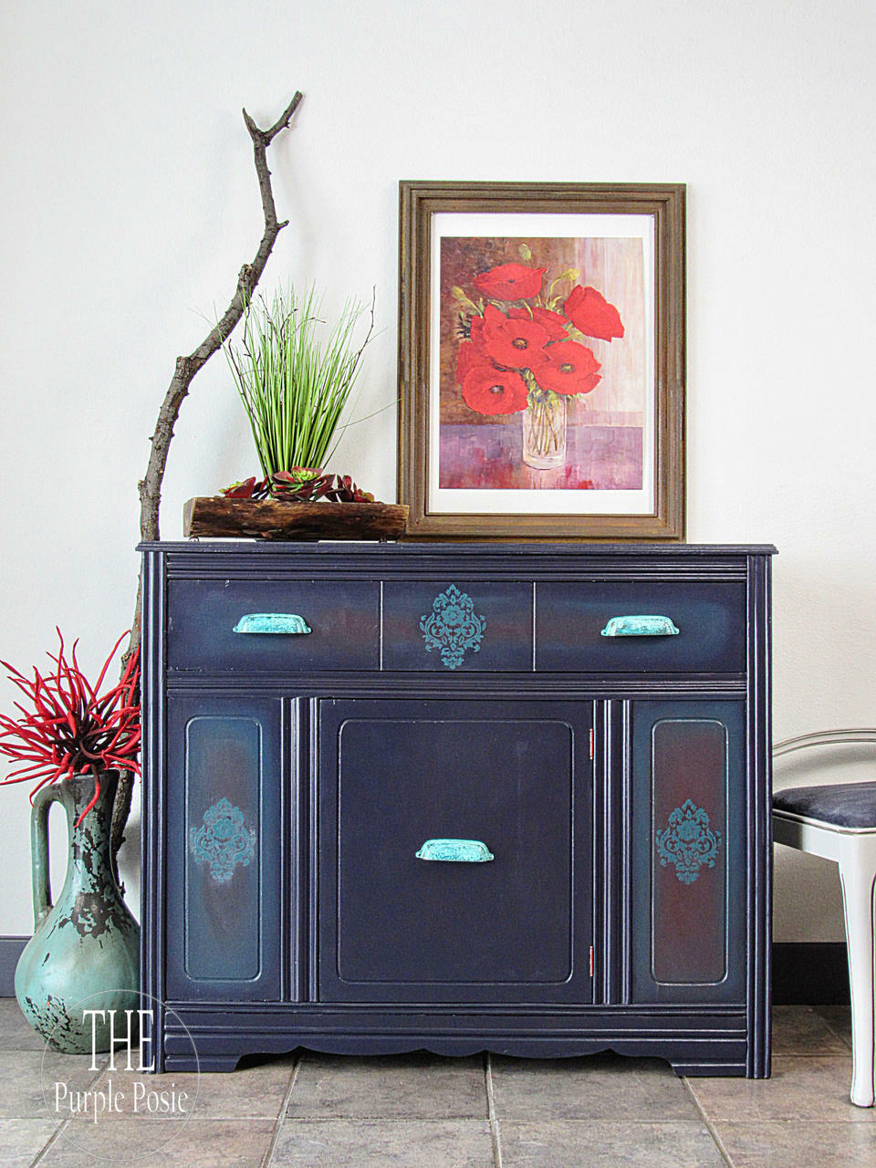 Belles and Whistles Floral - Silkscreen Stencil provides an extra decorative touch to your project!
A credenza piece with the flat panels using Floral - Silkscreen Stencil using a light blue paint. Staged with a framed picture of red flowers on top of the piece, along with a large branch and some greenery.