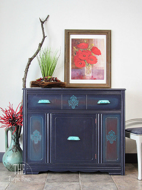 Belles and Whistles Floral - Silkscreen Stencil provides an extra decorative touch to your project!
A credenza piece with the flat panels using Floral - Silkscreen Stencil using a light blue paint. Staged with a framed picture of red flowers on top of the piece, along with a large branch and some greenery.