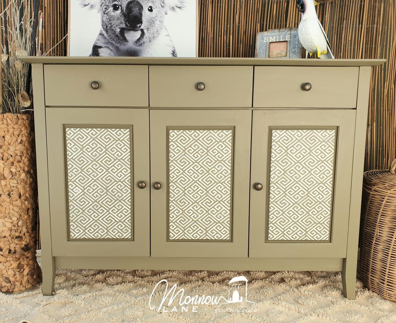 Belles and Whistles Greek Key - Stencil provides an extra decorative touch to any project! Tan colored vanity with Greek Key - Stencil on front of doors with bronze hardware. Staged on off-white carpet with brown wall, parrot statue with picture frame on right side and a picture frame of a koala on left side on top of dresser.