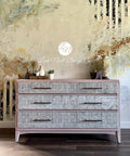 Belles and Whistles Greek Key - Stencil provides an extra decorative touch to any project! Tan colored wide dresser with Greek Key - Stencil on front of drawers, with brown hardware. Staged on a wooden floor with various miniature flower pots on each side on top of dresser.