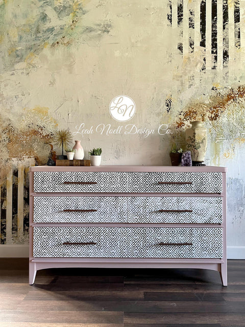 Belles and Whistles Greek Key - Stencil provides an extra decorative touch to any project! Tan colored wide dresser with Greek Key - Stencil on front of drawers, with brown hardware. Staged on a wooden floor with various miniature flower pots on each side on top of dresser.