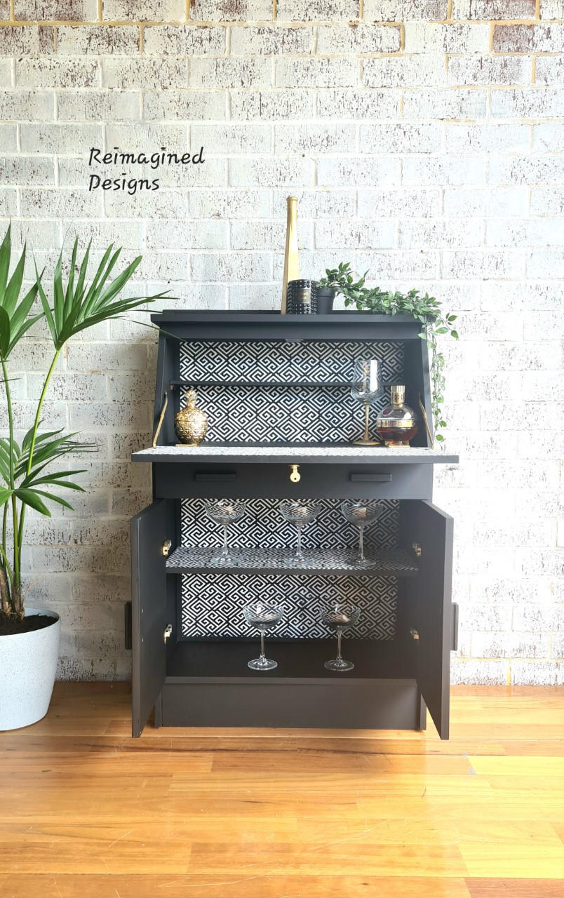 Belles and Whistles Greek Key - Stencil provides an extra decorative touch to any project! Black painted Bar cabinet staged with cabinet open with Greek Key - Stencil inside of piece. Staged with many wine glasses inside of furniture, and greenery staged on top of piece.