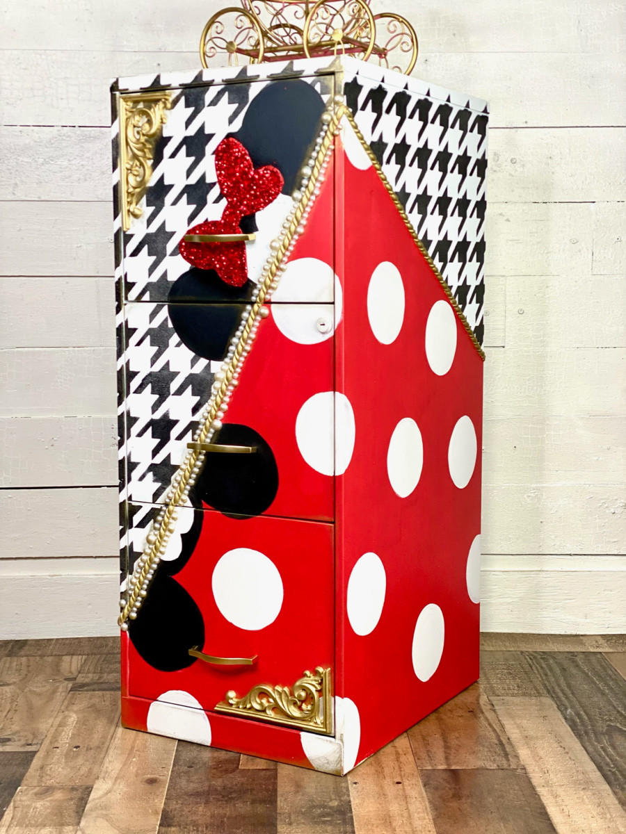 Belles and Whistles Houndstooth - Stencil provides an extra decorative touch to any project!
A file cabinet with half diagonally the cabinet in red with white polka dots and black mouse ears, on the other side is a white base with black Houndstooth - Stencil on top with black mouse ears with a red bow. In Between the two sides is a gold separator.