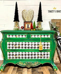 Belles and Whistles Houndstooth - Stencil provides an extra decorative touch to any project!
A green dresser with the drawers painted with a white base and Houndstooth - Stencil on top. Staged with Christmas whimsical decor on top and besides the furniture.