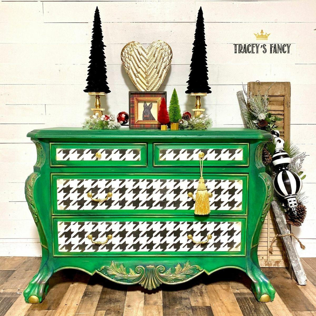 Belles and Whistles Houndstooth - Stencil provides an extra decorative touch to any project!
A green dresser with the drawers painted with a white base and Houndstooth - Stencil on top. Staged with Christmas whimsical decor on top and besides the furniture.