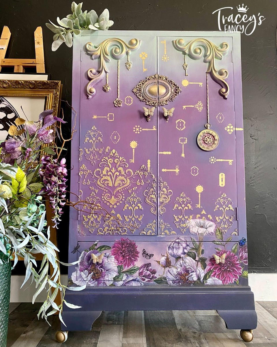 Large purple painted armoire with gold butterfly handles and accents. Buds & Branches Transfer applied on the bottom drawer. Royal Damask stencil applied in gold above the Transfer. Above the the Royal Damask stencil design, the Key to Success Stencil has been applied throughout the face of the armoire in gold.