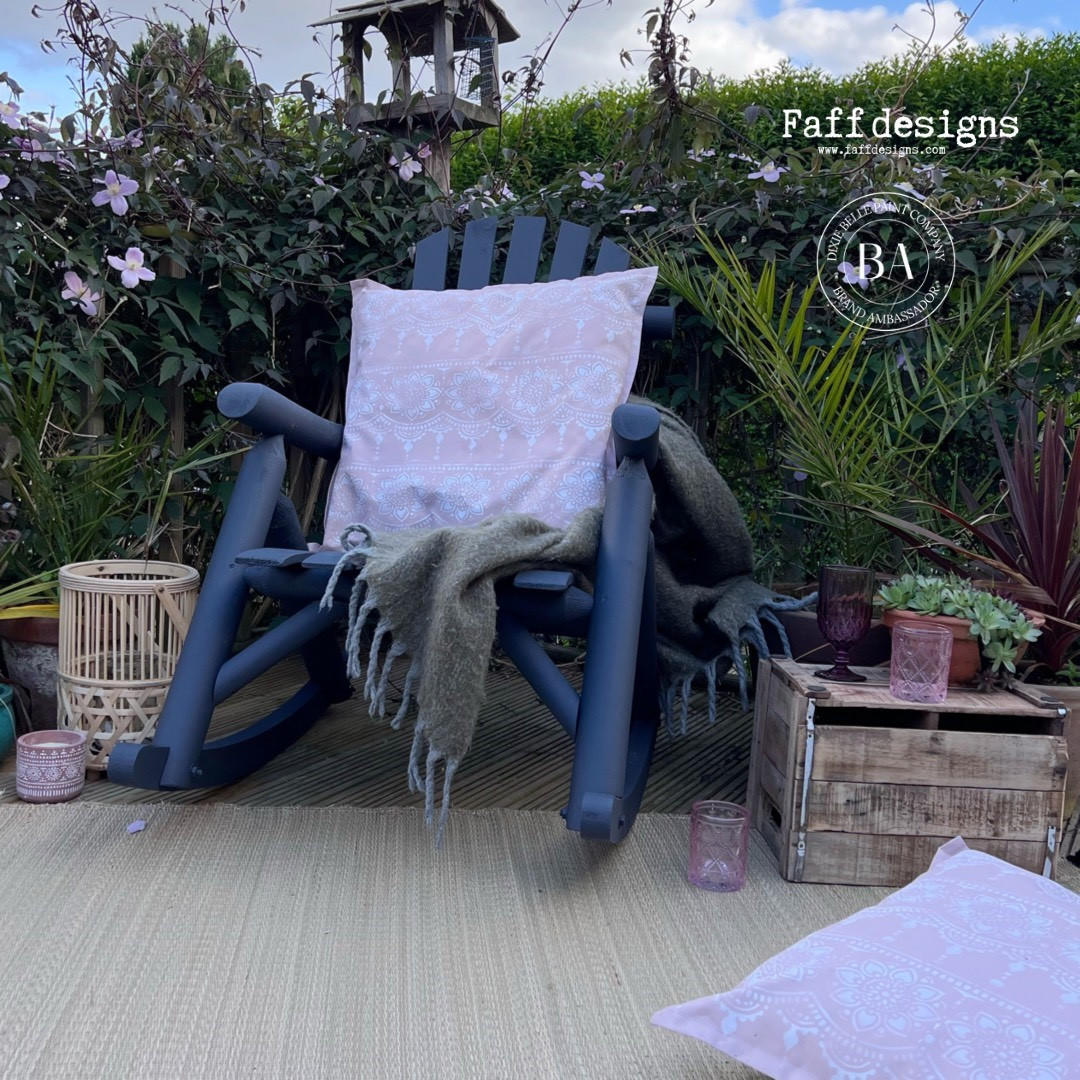 Belles and Whistles Lotus Bloom - Stencil provides an extra decorative touch to any project!
Image shows two light pink pillows with Lotus Bloom - Stencil used as the pattern on the fabric. One pillow is staged on top of a matte black rocking chair while the other is on the floor. Staged outside with greenery and wooden decor.