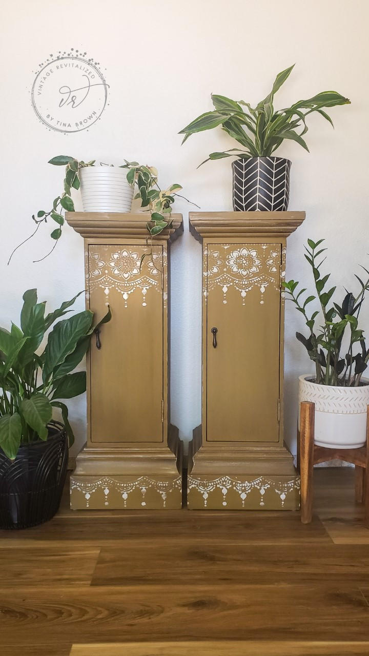 Belles and Whistles Lotus Bloom - Stencil provides an extra decorative touch to any project!
Two tan slender cabinet pillars with Lotus Bloom - Stencil in white at the top and base of furniture. Staged with flower pots on each side and on top of both pieces with greenery.