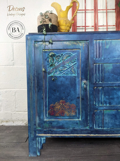 Belles and Whistles Mandala - Silkscreen Stencil provides an extra decorative touch to any project! Dark Blue Chalk Painted dresser door with a painted on Mandala Silkscreen Stencil. Staged with a wicker basket with plant and a yellow vase ontop.
