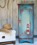 Belles and Whistles Nautical - Silkscreen Stencil provides an extra decorative touch to any project! Blue and red chalk painted armoire with a light house and ship wheel stenciled on. Staged next to a white luggage.