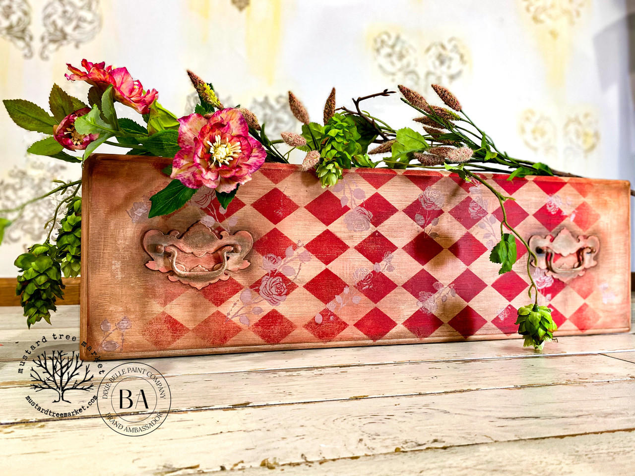 Belles and Whistles Roses - Silkscreen Stencil provides an extra decorative touch to any project! A leather case with a red diamond stencil on the front and top with the rose stencil painted lightly in white. The case is staged with flowers on top.