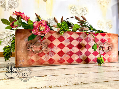 Belles and Whistles Roses - Silkscreen Stencil provides an extra decorative touch to any project! A leather case with a red diamond stencil on the front and top with the rose stencil painted lightly in white. The case is staged with flowers on top.