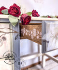 Belles and Whistles Roses - Silkscreen Stencil provides an extra decorative touch to any project! A closeup of the side of the drawers on a desk. The vertical rose design in white is shown on the the drawer side, staged with roses on top of the desk.