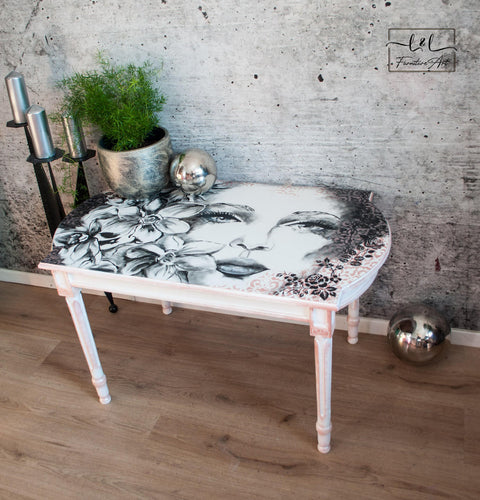 Belles and Whistles Roses - Silkscreen Stencil provides an extra decorative touch to any project! A table painted in white white a woman's face on top with succulents surrounding the left side and the rose stencil in black on the right side. The table is staged with greenery and candles on the left.