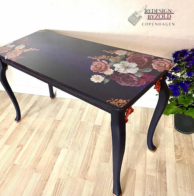 Belles and Whistles Roses - Silkscreen Stencil provides an extra decorative touch to any project! This image shows a black table with a flower transfer design on the right far side and also featuring our damask designed stencil in the corners on the top.