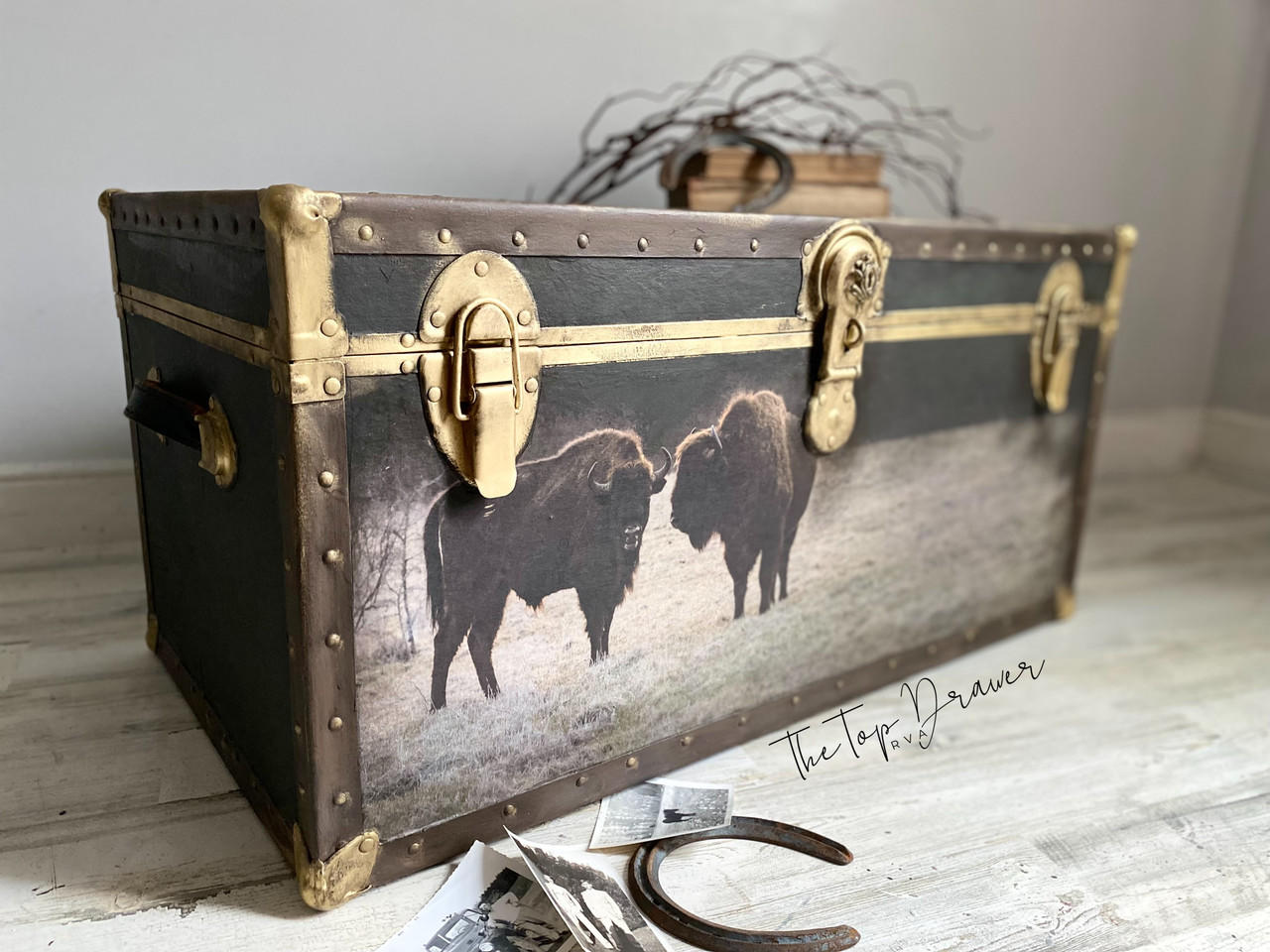 Belles and Whistles Tatanka - A1 Rice Decoupage Paper is a simple way to visually enhance any surface of your project! Large chest with leather on the edges and gold hinges and clasps. The Tatanka Rice Decoupage Paper has been applied on the front of the chest. There is newspaper clippings on the floor in front of the chest along with a rusty horseshoe.