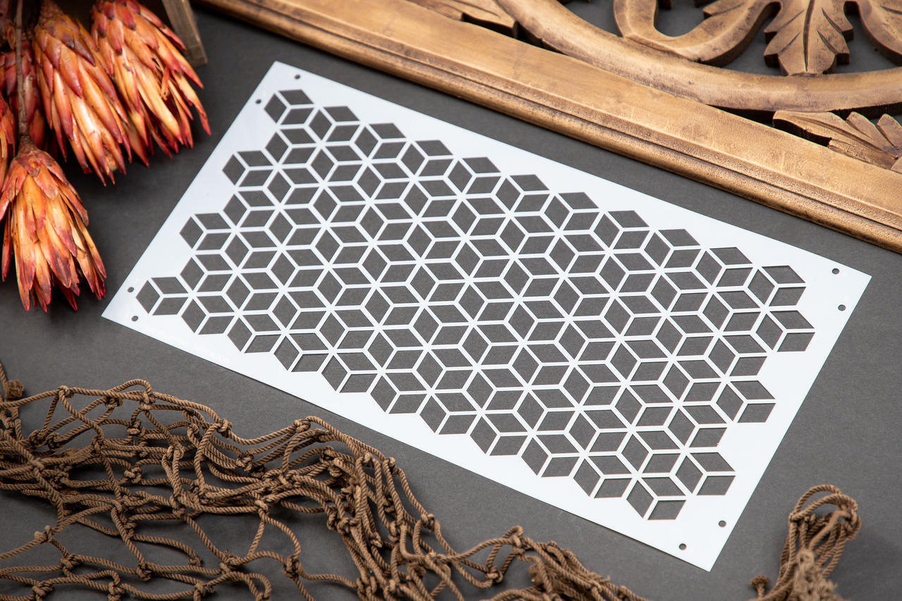 Belles and Whistles Trippy Blocks - Stencil provides an extra decorative touch to any project!  A picture of the Trippy Blocks stencil sitting on a black table with a brown net, brown flowers and a brown piece of wood around the stencil.