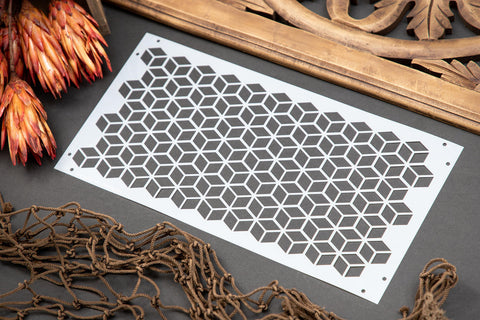 Belles and Whistles Trippy Blocks - Stencil provides an extra decorative touch to any project!  A picture of the Trippy Blocks stencil sitting on a black table with a brown net, brown flowers and a brown piece of wood around the stencil.