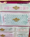 Belles and Whistles Trippy Blocks - Stencil.  The right side of a pink, blue and white dresser.  the handles are painted gold, and there is gold trim and gold spots on the dresser.  The drawers are blue and pink with white chalk paint dry brushed over the stenciled patterns.