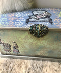 Belles and Whistles Victorian Damask - Stencil provides an extra decorative touch to any project!  A blue and green chalk painted blanket chest sits on a white shag rug.  The Victorian Damask Stencil is chalk painted in white, blue, yellow and pink on the top of the chest and in brown on the front of the chest.  The Alice transfer is applied to the top and front of the chest, and WoodUbend is applied to the top and folded over to the front and is chalk painted in yellow, brown and blue.