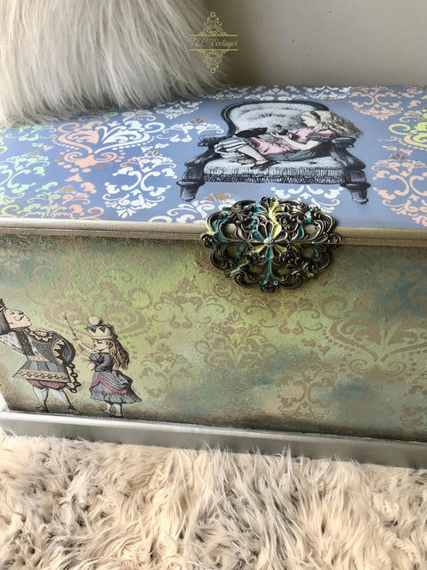 Belles and Whistles Victorian Damask - Stencil provides an extra decorative touch to any project!  A blue and green chalk painted blanket chest sits on a white shag rug.  The Victorian Damask Stencil is chalk painted in white, blue, yellow and pink on the top of the chest and in brown on the front of the chest.  The Alice transfer is applied to the top and front of the chest, and WoodUbend is applied to the top and folded over to the front and is chalk painted in yellow, brown and blue.