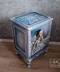 Belles and Whistles Victorian Damask - Stencil provides an extra decorative touch to any project!  A small blue and white chalk painted night stand with a picture of a young girl in a white dress applied as a decoupage to the front.  The Victorian Damask stencil is applied to the top and side with white Chalk Paint.  Staged on a brown wooden floor, in front of a gray wall with white wooden trim.