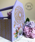Belles and Whistles Western Boho - Silkscreen Stencil provides an extra decorative touch to any project!  A purple chalk painted magazine floor rack with the Western Boho Silkscreen Stencil applied to the front and sides with gold paint.  A muti colored succulent transfer is applied to the front.  The rack sits on a light colored wooden floor with pink and purple flowers to the right of it.