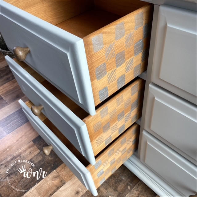 Belles and Whistles Whimsical Check - Stencil provides an extra decorative touch to any project!  Part of a gray chalk painted dresser with 3 drawers partially open.  The sides of all 3 drawers have the Whimsical Check stencil chalk painted on them in silver metallic paint.  Sitting on a multicolored brown wooden floor.