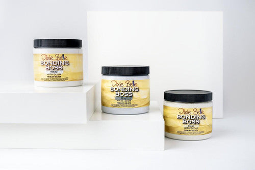 Three jars of Dixie Belle Bonding Boss, a primer, are displayed on white geometric platforms against a plain white background. The jars are 16 oz. and feature yellow and white labels with black lids.