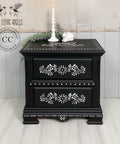 Elegant black painted nightstand with Bone Inlay Stencil applied with floral patterns and decorative details, featuring a candle and small ornaments atop, against a shiplap backdrop.