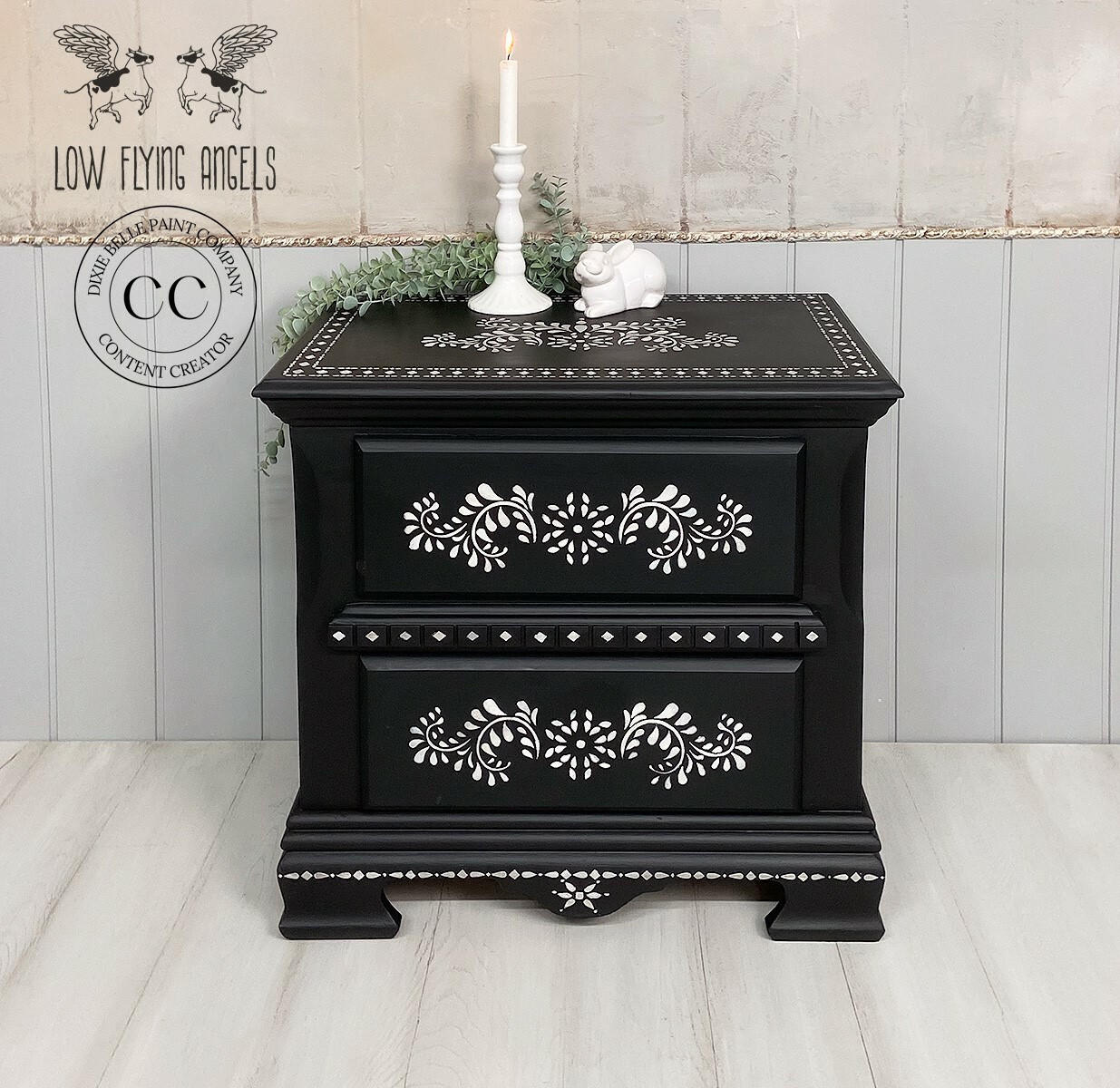 Elegant black painted nightstand with Bone Inlay Stencil applied with floral patterns and decorative details, featuring a candle and small ornaments atop, against a shiplap backdrop.