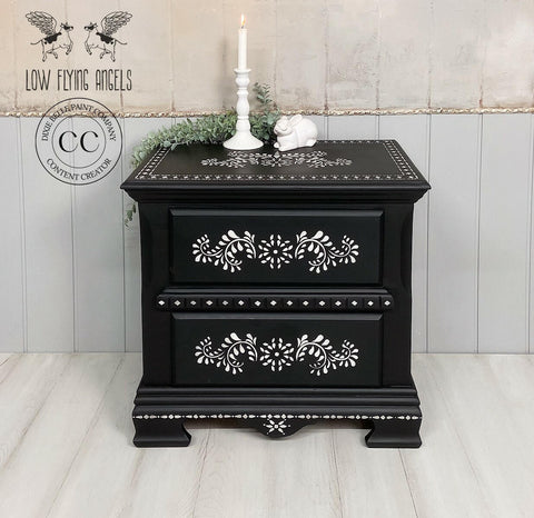 Elegant black painted nightstand with Bone Inlay Stencil applied with floral patterns and decorative details, featuring a candle and small ornaments atop, against a shiplap backdrop.