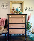 A vintage dresser with light wood drawers and dark frame is topped with books, globes, and a clock. An empty ornate frame hangs above. A plant, pink scarf, and hat decorate the scene. Logos on the wall read â€œDixie Belle Paint Company Content Creatorâ€ and â€œby Melinda MTZ Crew Designsâ€.
