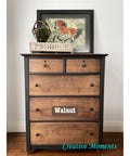 A wooden dresser with the word "Walnut" on one of the drawers. On top, there's a framed picture of a horse and a sign that reads "Produce." The floor is wooden, and the wall is plain white. "Creative Moments" is written in blue on the floor.