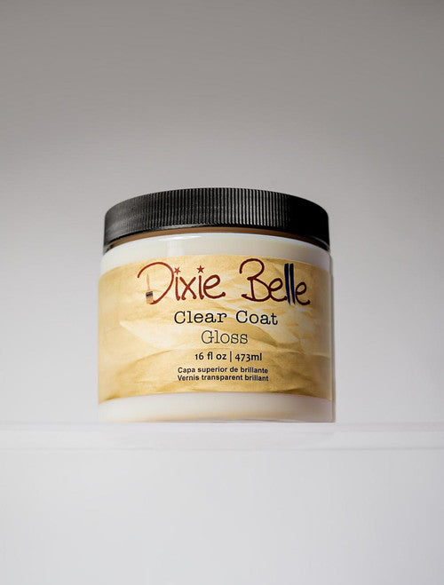 A jar of Dixie Belle Clear Coat Gloss with a black lid and beige label, containing 16 fl oz (473 ml) of product, is displayed against a plain, light background.