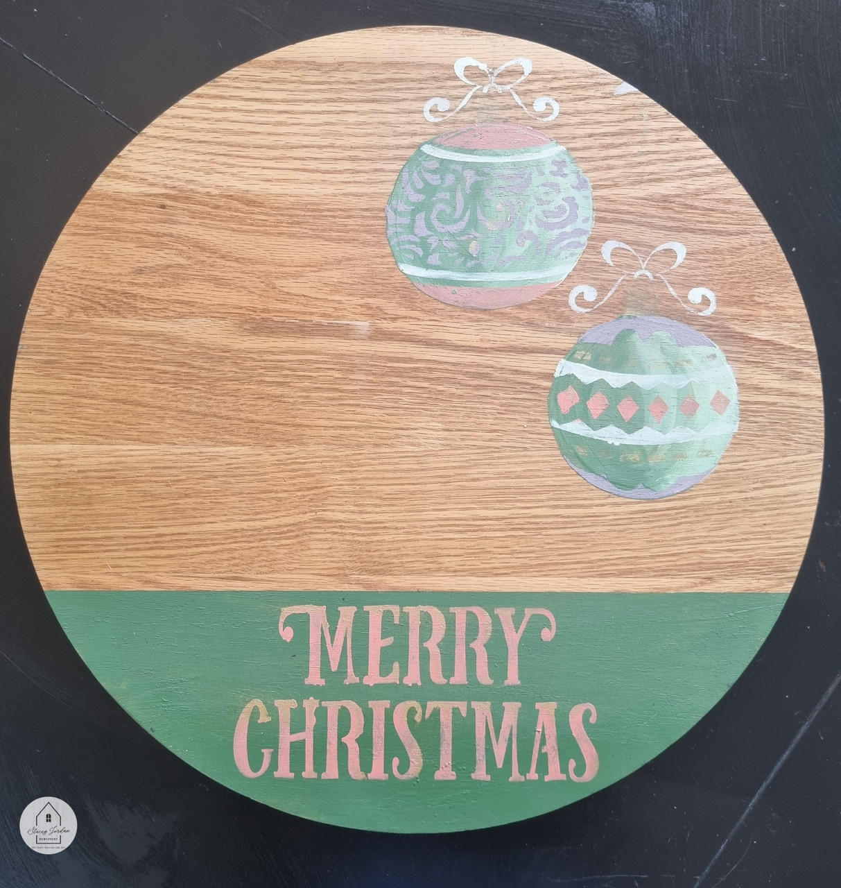 Wooden circular board with "Merry Christmas" from the Christmas Cheer stencil on the bottom applied in pink over green chalk paint. Two ornaments were applied with green, pink, purple, and white chalk paint from the Holiday Joy stencil.
