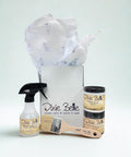 A set of Dixie Belle paint products, including a spray bottle, one small jar of Caviar paint, a paint brush, and a jar of clear coat, displayed in front of an open box with tissue paper.