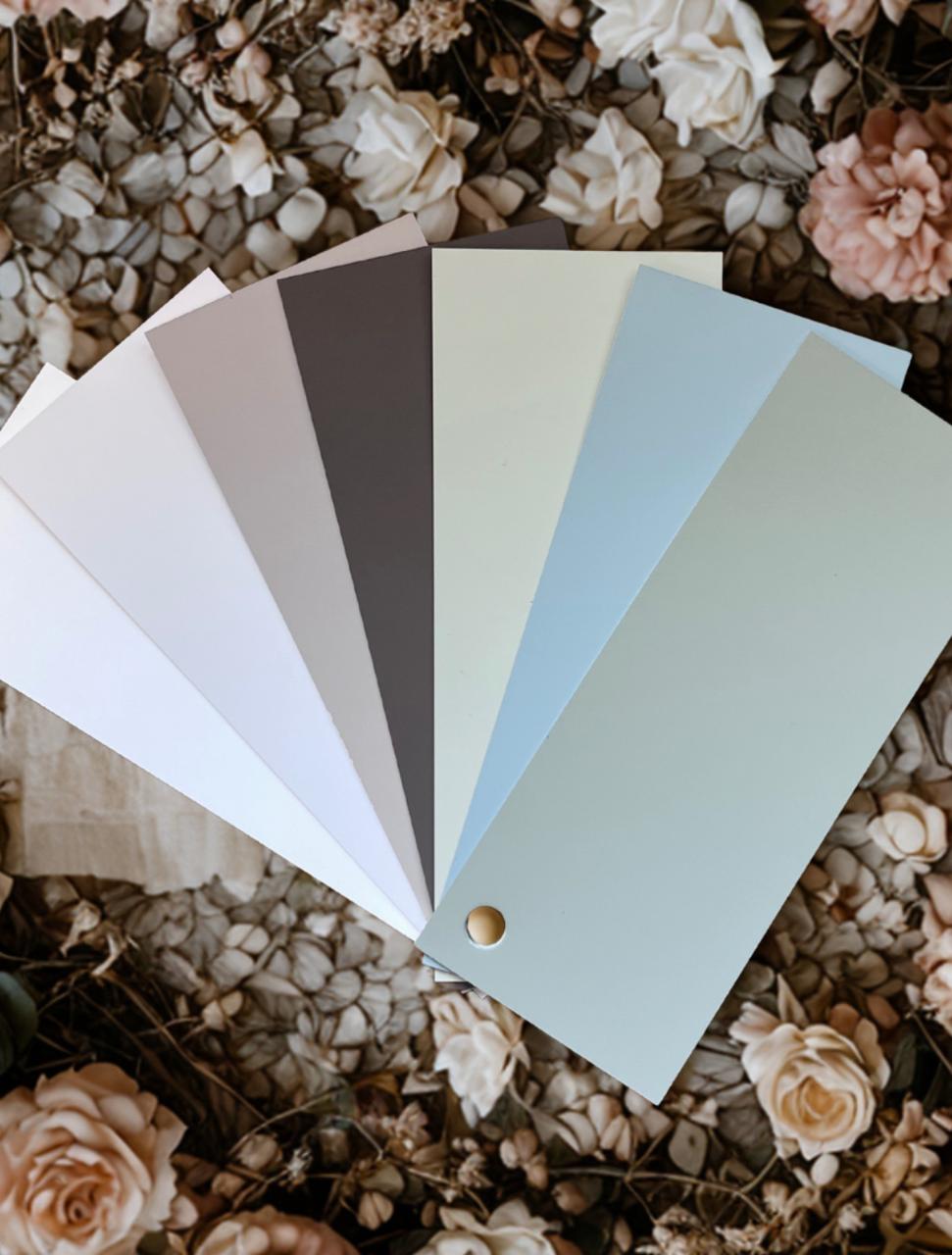 A fan of six paint swatches in neutral and pastel shades arranged over a floral background with beige and blush pink flowers.