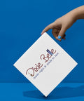 A hand with blue nail polish holds a white square box against a blue background. The box reads "Dixie Belle made right &amp; made to last" in stylized text.