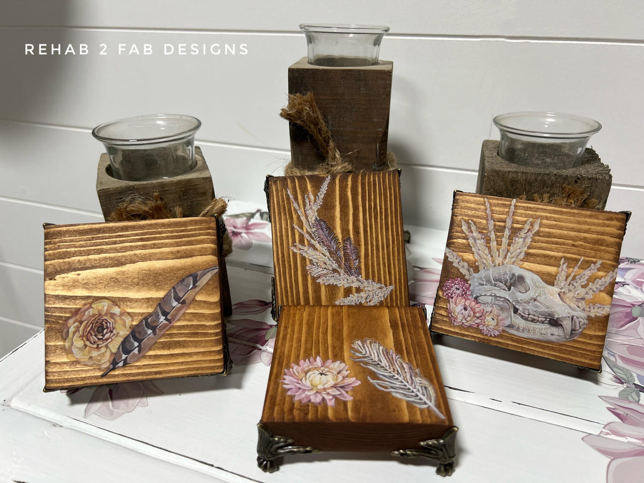 Wooden decor pieces featuring floral and feather designs, from the Desert Moon Transfer, are displayed on a white surface. Two wooden holders with glass candle cups are in the background. The text "REHAB 2 FAB DESIGNS" is visible in the top left corner.