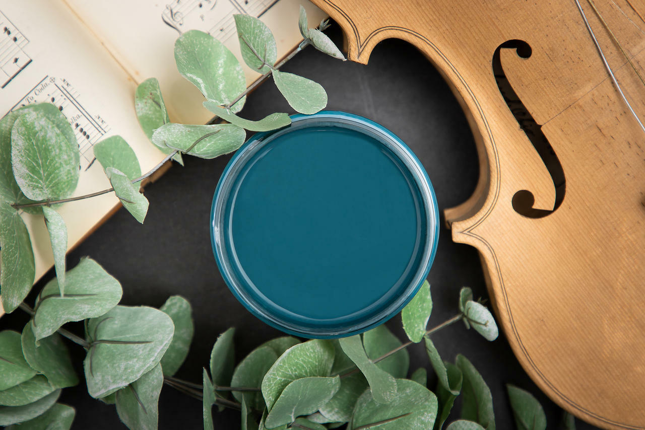 Dixie Belle Paint Antebellum Blue Chalk Mineral Paint is the perfect paint for any DIY project! Open container of Antebellum Blue Chalk Mineral Paint against black background with cello and music sheet.