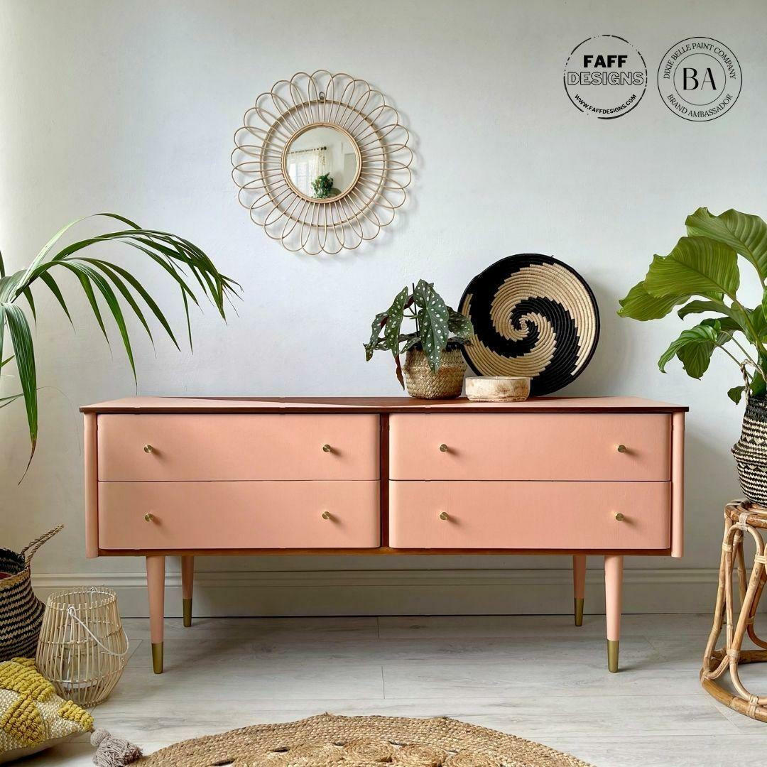 Dixie Belle Paint Apricot Chalk Mineral Paint is the perfect paint for any DIY project!
Console table with drawers painted in Apricot Chalk Mineral Paint along with gold hardware. Staged with greenery and woven decors like bowls, baskets and plant pots around the table.