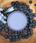Dixie Belle Paint Blueberry Chalk Mineral Paint is the perfect paint for any DIY project!
Aerial view of opened container of Blueberry Chalk Mineral Paint staged on top of wooden circular board with blueberries and flower around container.