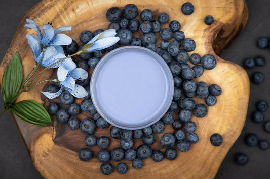 Dixie Belle Paint Blueberry Chalk Mineral Paint is the perfect paint for any DIY project!
Aerial view of opened container of Blueberry Chalk Mineral Paint staged on top of wooden circular board with blueberries and flower around container.