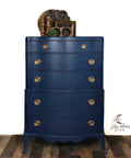 Dixie Belle Paint Bunker Hill Blue Chalk Mineral Paint is the perfect paint for any DIY project!
Chest of drawer painted in Bunker Hill Blue Chalk Mineral Paint with gold hardware and brown wooden decor on top of the piece. Staged in front of a white wall and brown wooden floors.