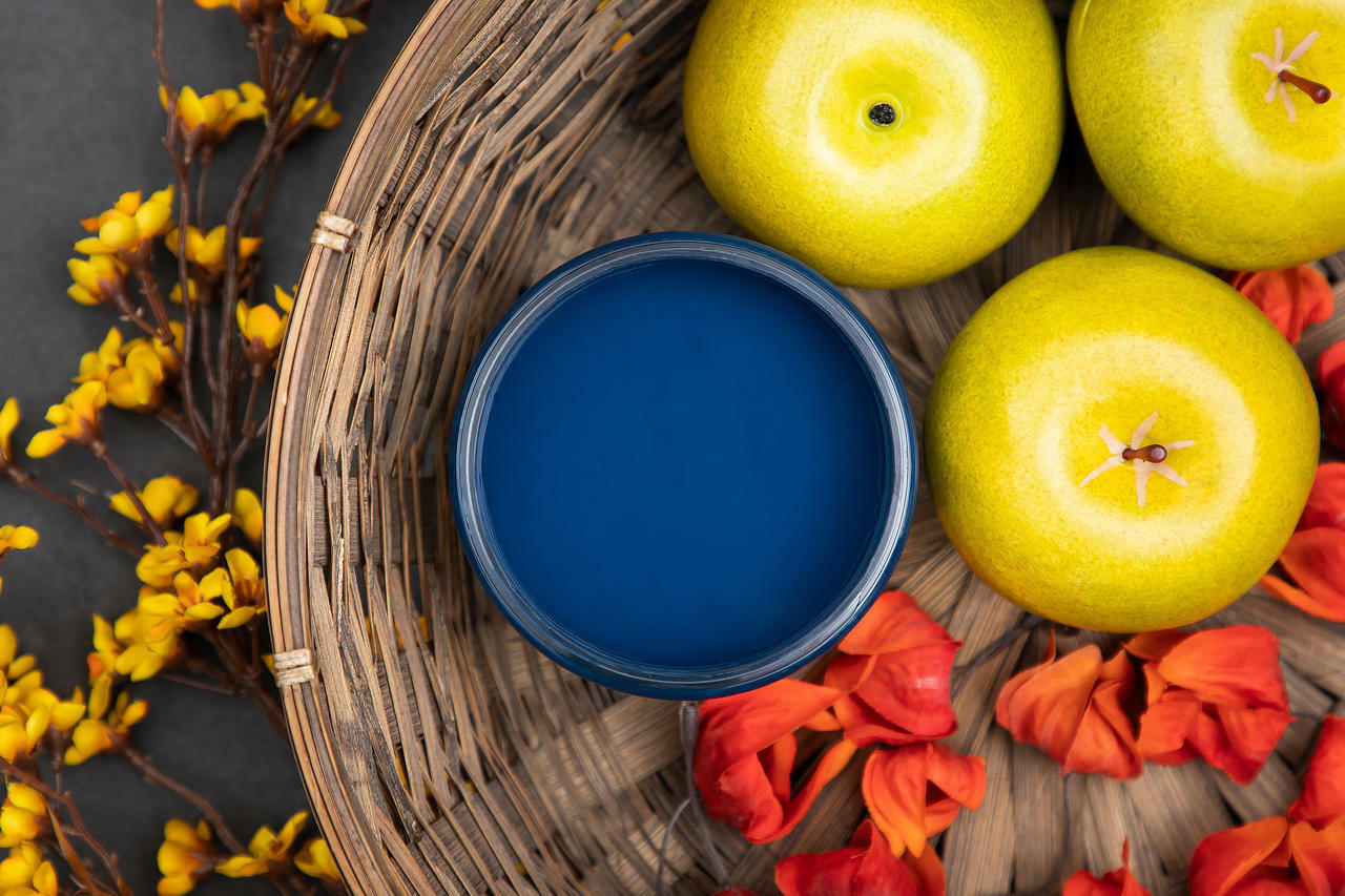 Dixie Belle Paint Bunker Hill Blue Chalk Mineral Paint is the perfect paint for any DIY project!
The opened container of Bunker Hill Blue Chalk Mineral Paint staged with yellow apples and pink-orange flower petals inside a woven basket and yellow flowers on a branch outside the basket.