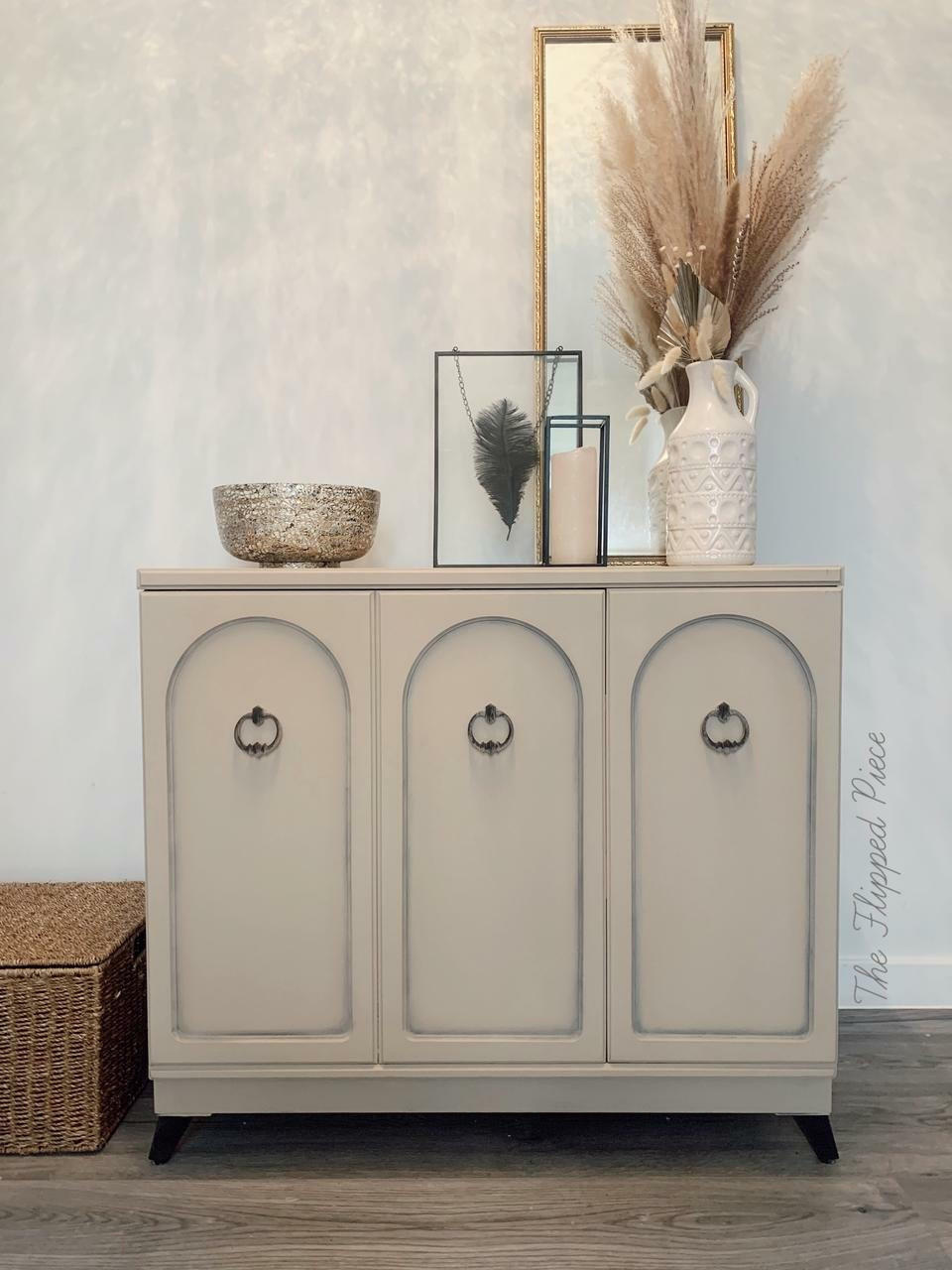 Dixie Belle Paint Burlap Chalk Mineral Paint is the perfect paint for any DIY project!
A 3 door cabinet painted in Burlap Chalk Mineral Paint with black hardware, staged with frames and a bowl on top of the piece.