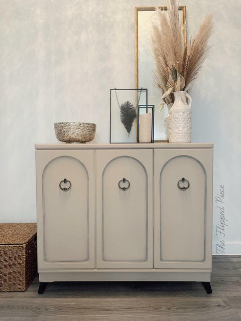 Dixie Belle Paint Burlap Chalk Mineral Paint is the perfect paint for any DIY project!
A 3 door cabinet painted in Burlap Chalk Mineral Paint with black hardware, staged with frames and a bowl on top of the piece.