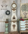 Dixie Belle Paint Burlap Chalk Mineral Paint is the perfect paint for any DIY project!
A mora clock painted in Burlap Chalk Mineral Paint also using the Patina line around the the edges of the piece to give an antique style. Staged with a mint green pedestal with bronze books on top to the left side of the clock and a large canvas with a potted tree on top of a matching dresser.