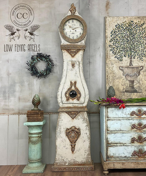 Dixie Belle Paint Burlap Chalk Mineral Paint is the perfect paint for any DIY project!
A mora clock painted in Burlap Chalk Mineral Paint also using the Patina line around the the edges of the piece to give an antique style. Staged with a mint green pedestal with bronze books on top to the left side of the clock and a large canvas with a potted tree on top of a matching dresser.